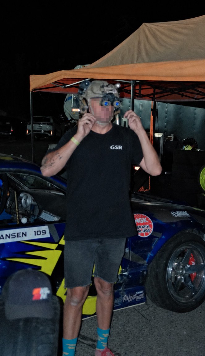 Man in a GSR tee putting on a night vision helmet at a drift event